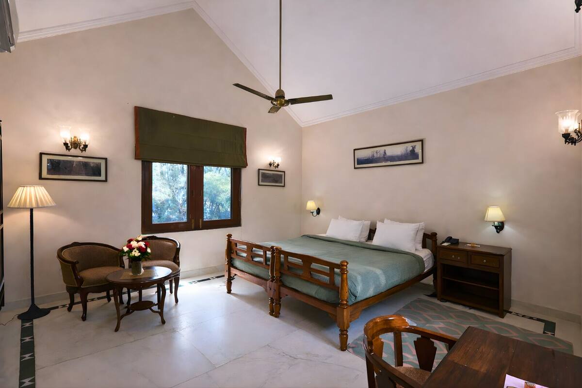 A bedroom with a bed, a chair, a table, a standing lamp, and a ceiling fan.