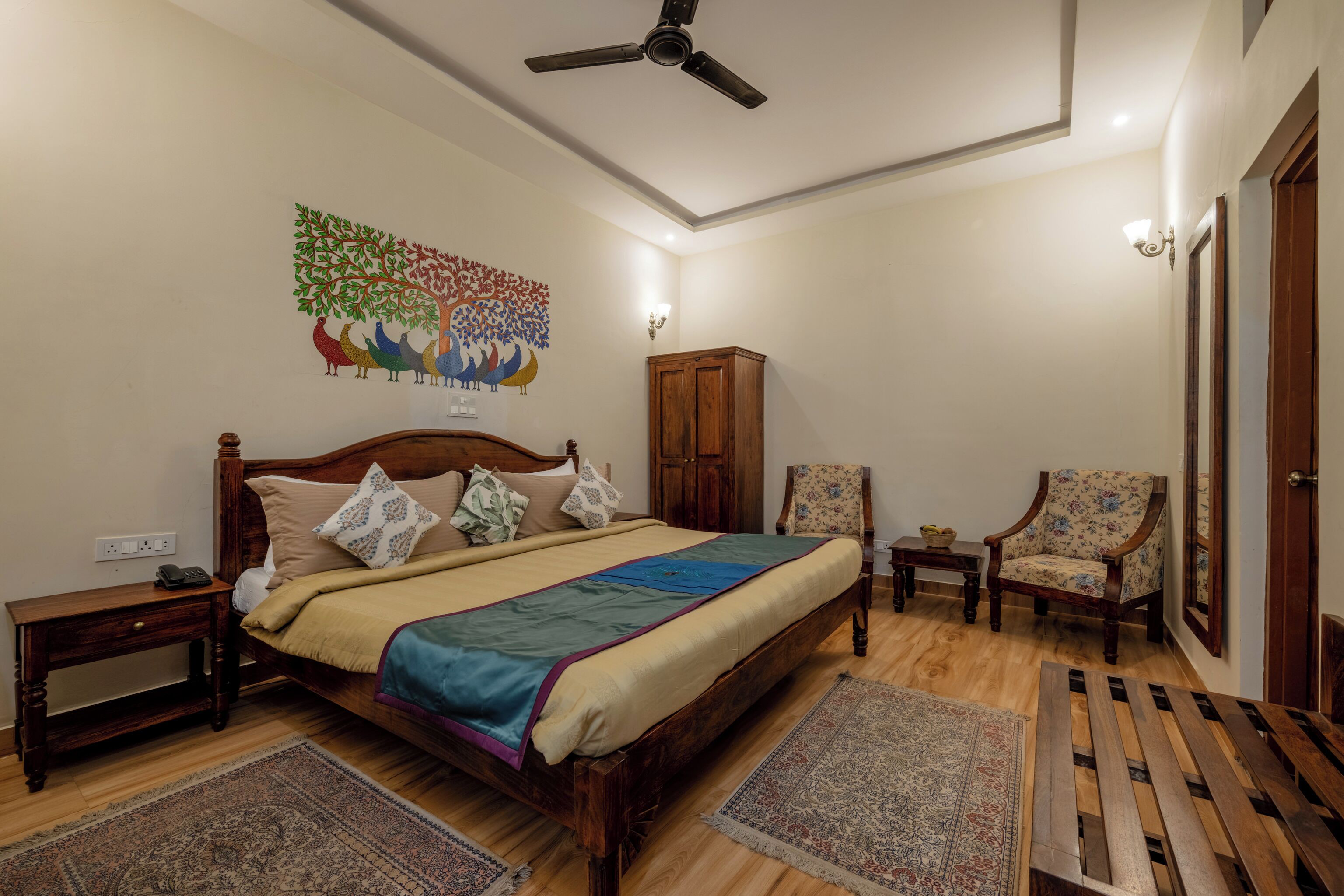 A bedroom with a bed, two chairs, a wardrobe, a nightstand, and a ceiling fan.
