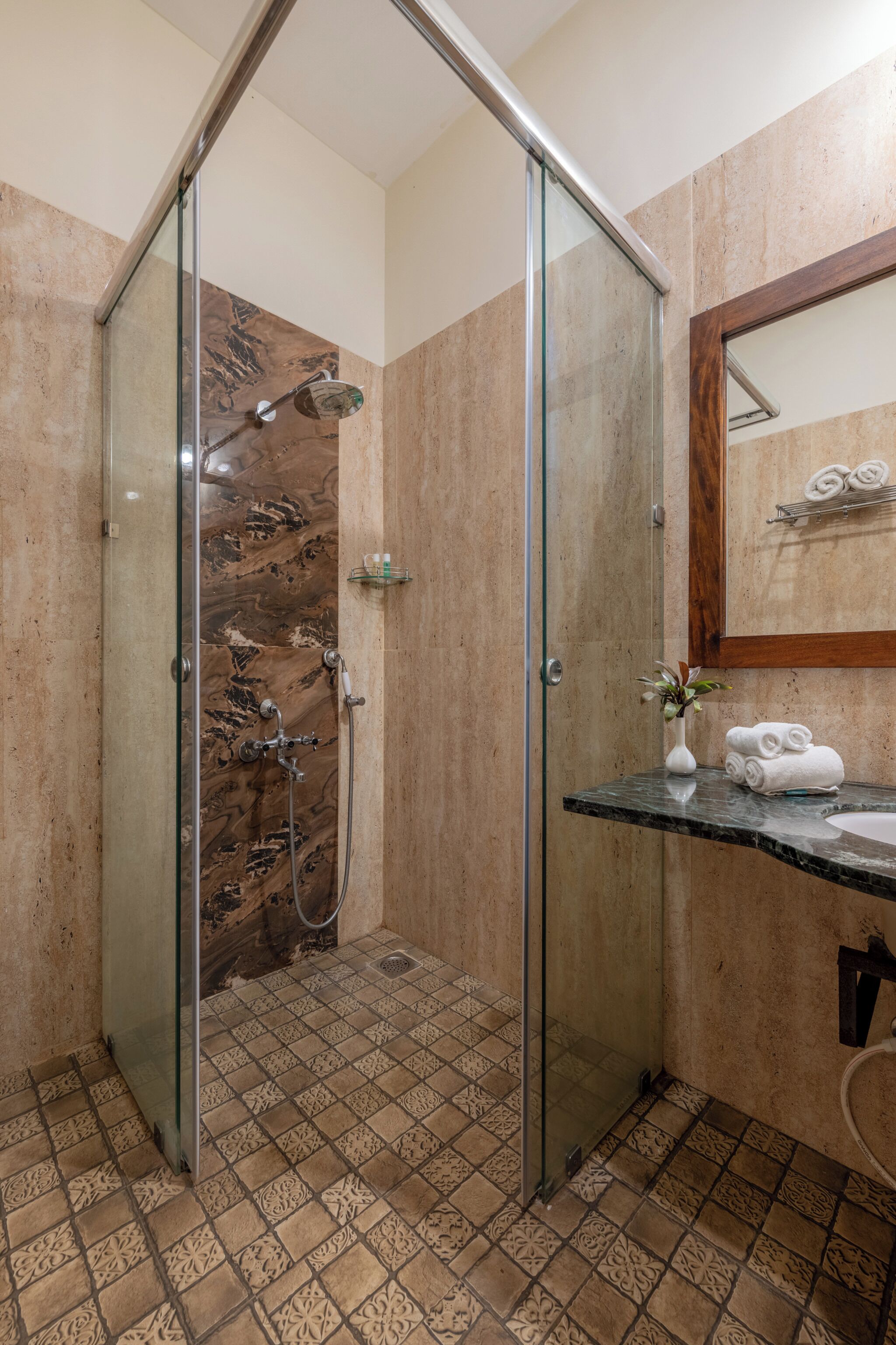 A modern bathroom with a glass shower enclosure, a marble-tiled shower area, a marble countertop, and a sink with a mirror above it.