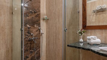 A modern bathroom with a glass shower enclosure, a marble-tiled shower area, a marble countertop, and a sink with a mirror above it.