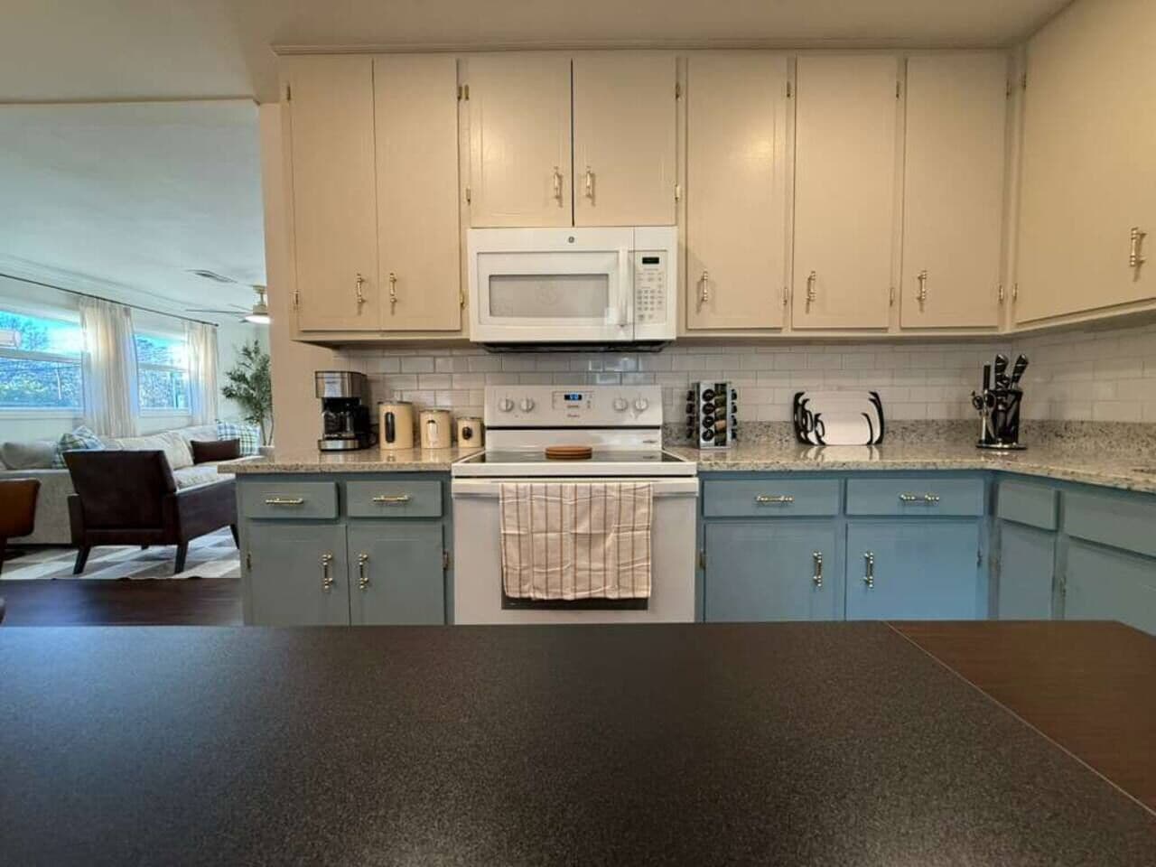 Een keuken met lichtblauwe kastjes, een witte magnetron en een fornuis.