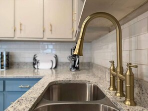 A kitchen with a stainless steel sink, a gold faucet, and a marble countertop. - CHIC OASIS - Pool - Games - Pet friendly, 15 mins to Fort Bening (Columbus)