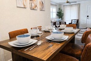 A dining area with a wooden table set for six, including bowls, plates, and wine glasses. - CHIC OASIS - Pool - Games - Pet friendly, 15 mins to Fort Bening (Columbus)