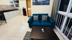 A living room with a blue sofa, a coffee table, and a painting of a night sky. - 1BR Service Apart Parel 3504 Near TMH By Florastays (Mumbai)