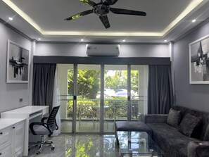 Ein modernes Wohnzimmer mit Glastisch, grauem Sofa und Deckenventilator.