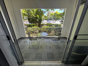 Ein Balkon mit einem Metalltisch und zwei Stühlen, Blick auf parkende Autos und Grünflächen.