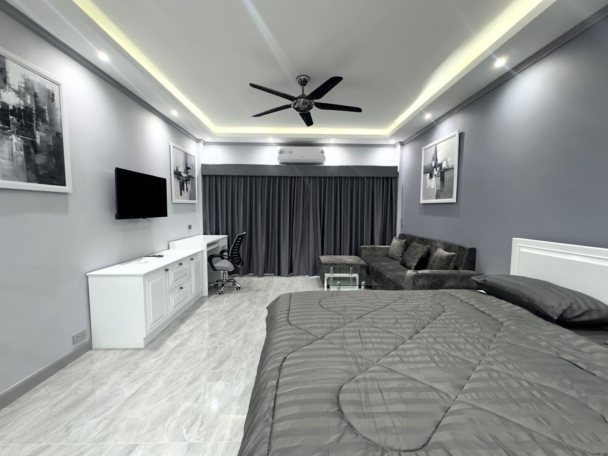 Um quarto moderno com uma cama grande, uma escrivaninha, uma cadeira, um sofá e um ventilador de teto.