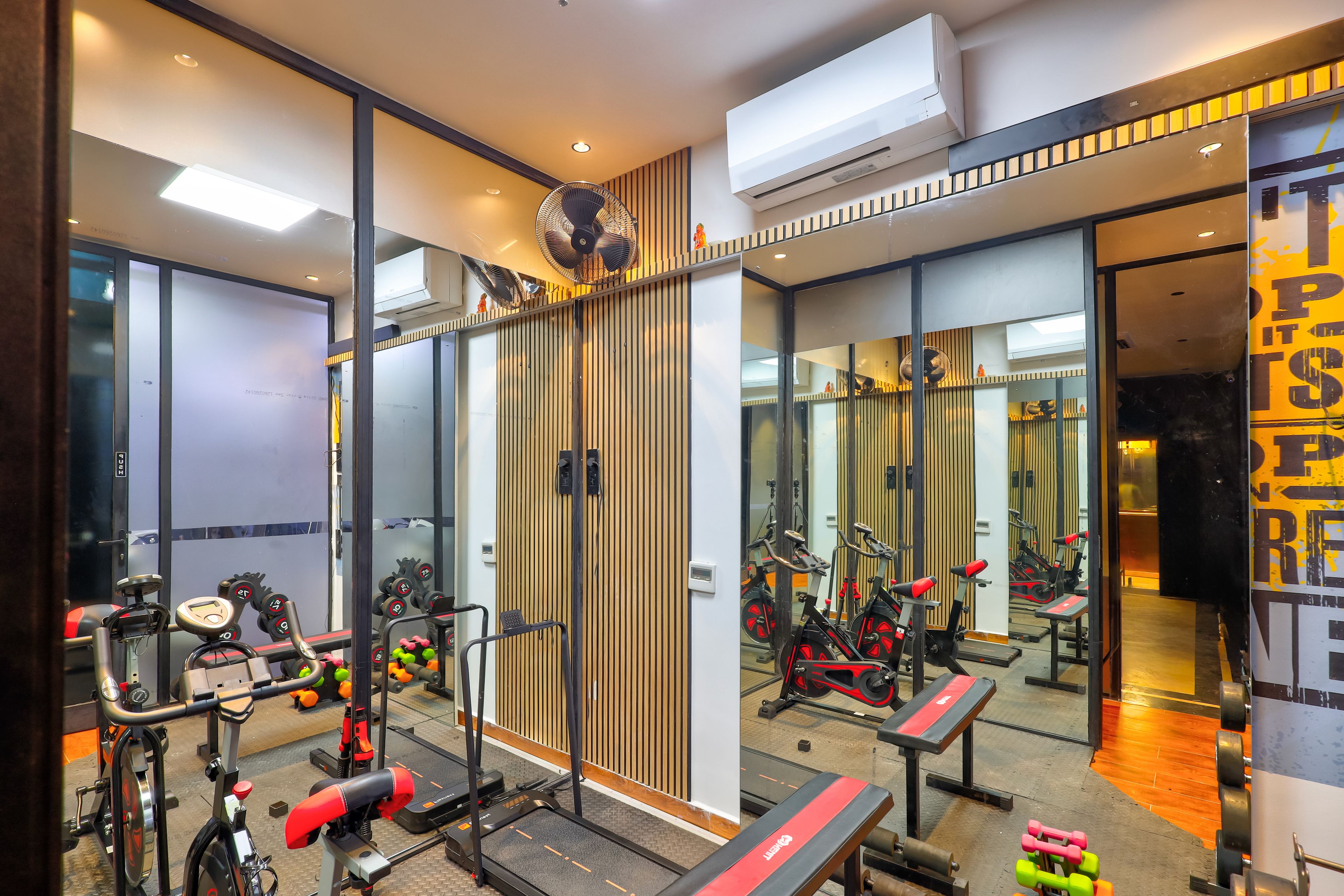 Un gimnasio con equipo de ejercicio, espejos y una pared de madera.