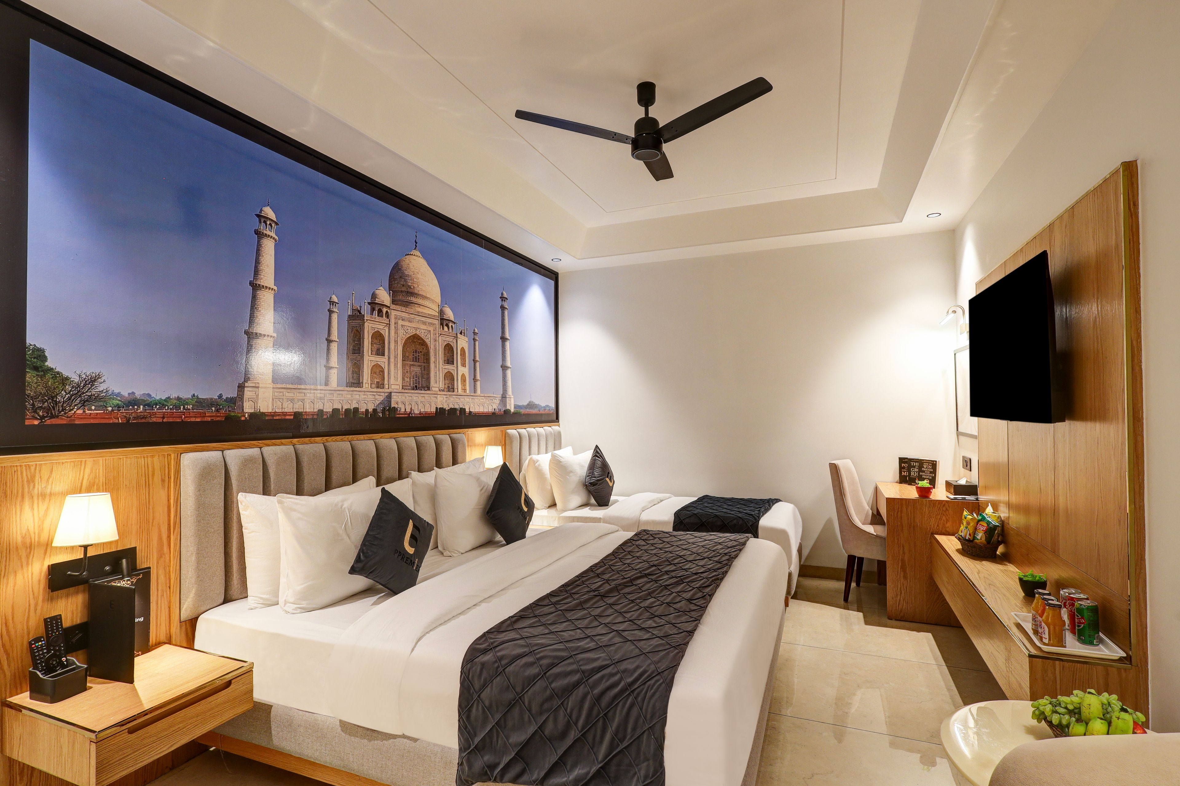 A hotel room with a large wall mural of the Taj Mahal, a bed with multiple pillows, a desk with a lamp, and a flat-screen TV.