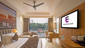 A hotel room with a bed, a desk, a chair, a sofa, a TV, and a view of the outside. - Hotel Premier Inn (New Delhi)