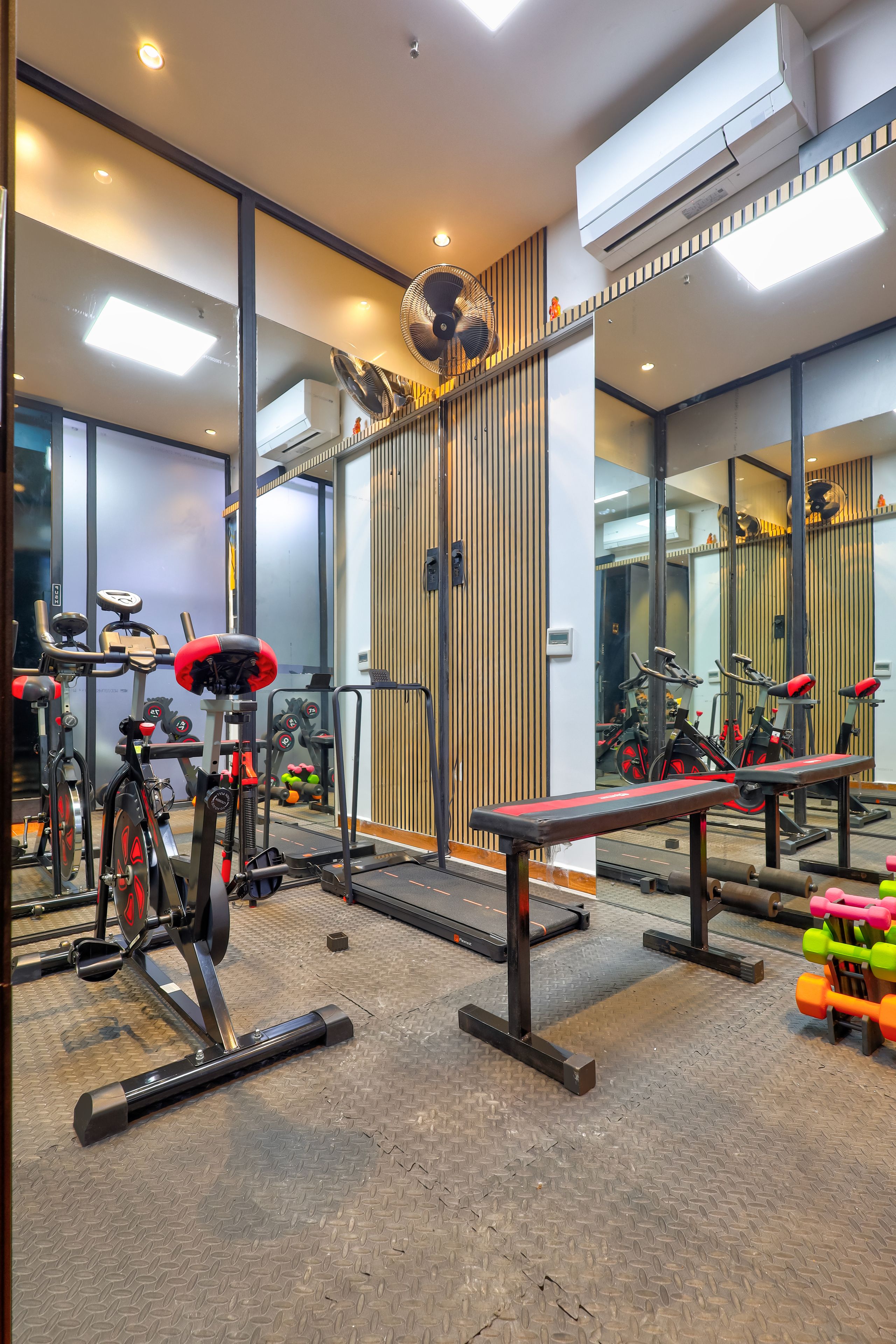 A gym with exercise equipment, mirrors, and a ventilation system.