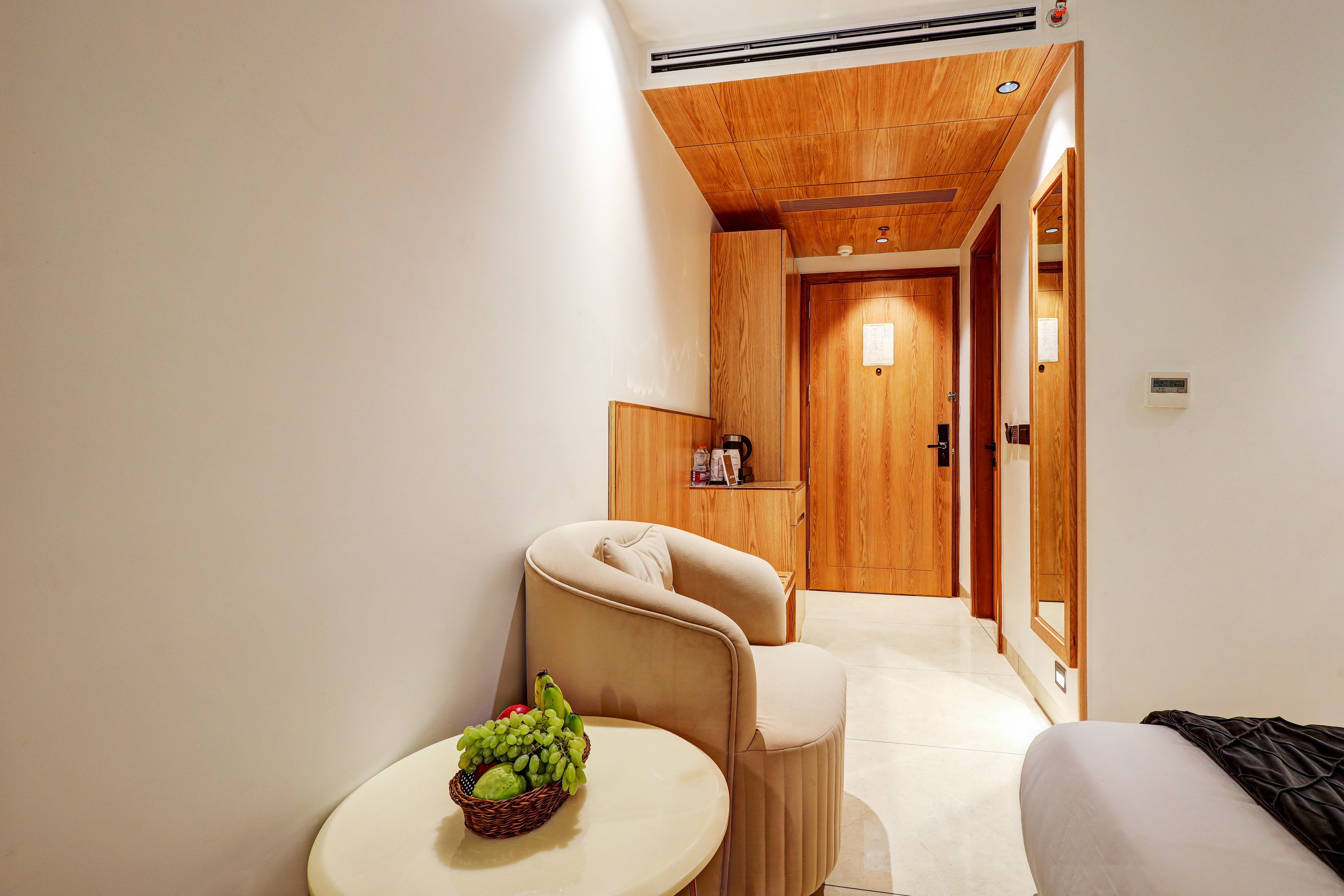 Une chambre d’hôtel avec un plafond en bois, une petite table ronde sur laquelle se trouve un panier de fruits, un fauteuil beige et un lit recouvert d’une couverture noire.