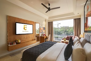 A hotel room with a large bed, a television mounted on the wall, a ceiling fan, and a window with a view of the outside. - Hotel Premier Inn (New Delhi)