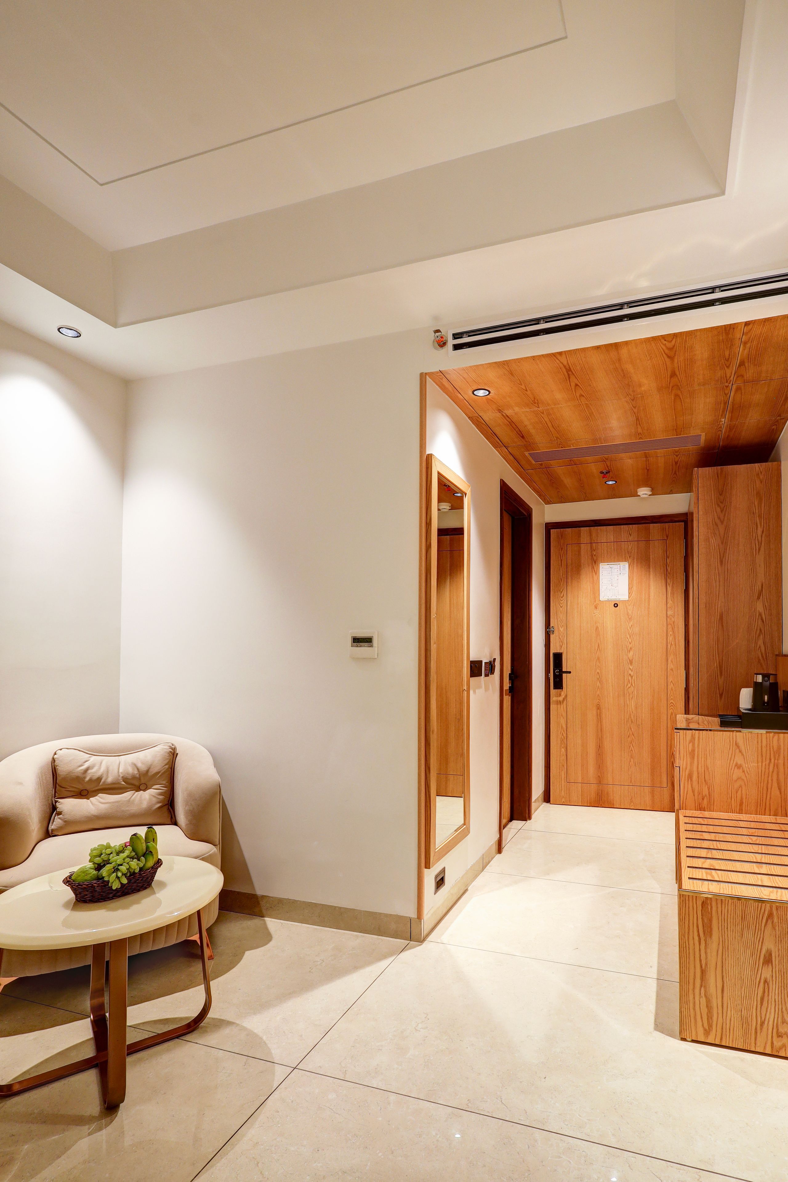 Una habitación con un sofá, una pequeña mesa redonda con una cesta de frutas, un armario de madera y una puerta que da a otra habitación.