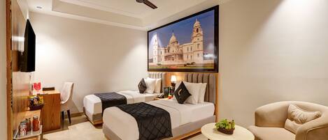 A hotel room with two beds, a desk, a chair, a small table with a plant, and a ceiling fan.