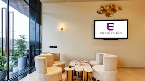 A modern hotel lobby with a large window, a reception desk, and a seating area with round tables and chairs. - Hotel Premier Inn (New Delhi)