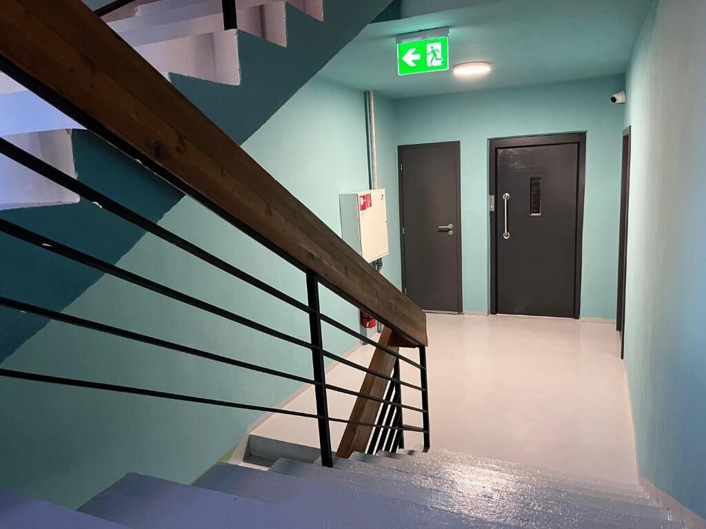 A staircase with a wooden handrail and metal balusters, leading to a room with a teal wall and a door with a handle.