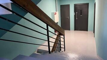 Una escalera con barandilla de madera y balaustres de metal, que conduce a una habitación con pared verde aguamarina y una puerta con picaporte.