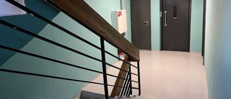 A staircase with a wooden handrail and metal balusters, leading to a room with a teal wall and a door with a handle.