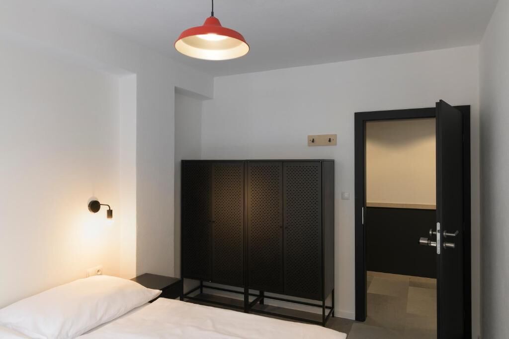 Une chambre à coucher comprenant un lit, une armoire, un miroir intégré à l’armoire et une lampe suspendue rouge.