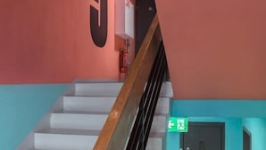 A staircase with a wooden handrail leading to a door marked with a green exit sign. - IZY STAY Hostel Bratislava (Bratislava)