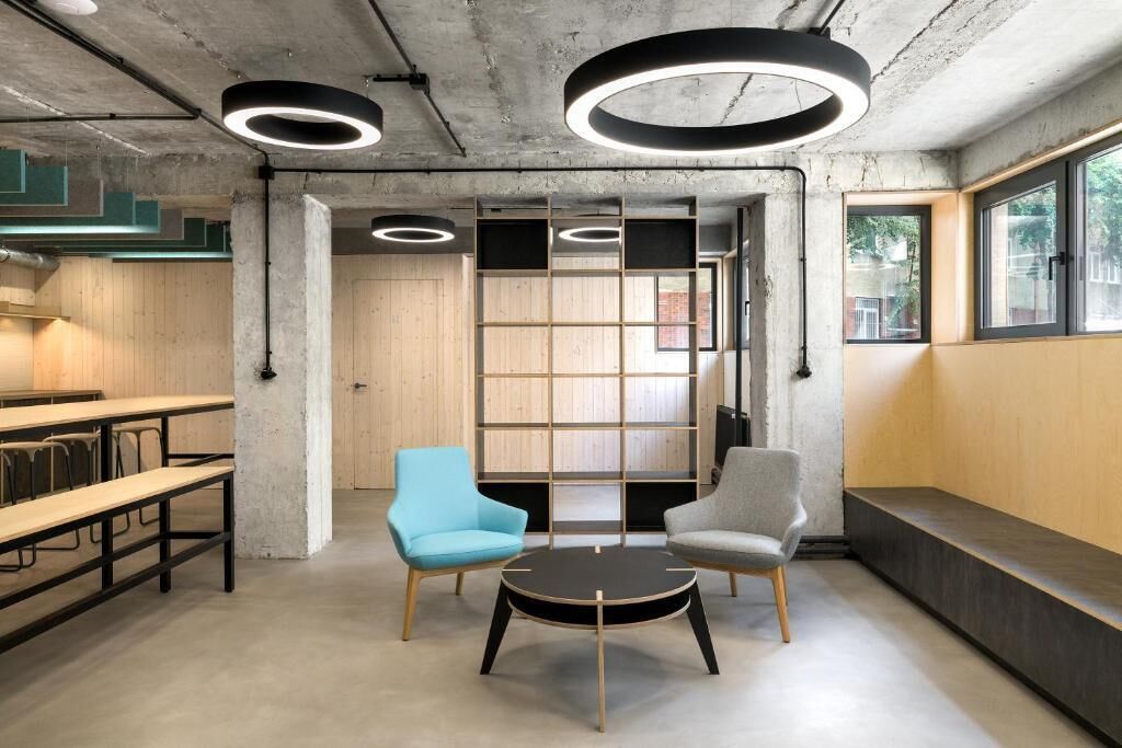 Un espace de bureau moderne avec des murs en béton, des panneaux de bois et un coin salon comprenant deux chaises et une table.