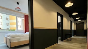 A modern hotel room with a bed, a large window, and a view of a building outside. - IZY STAY Hostel Bratislava (Bratislava)