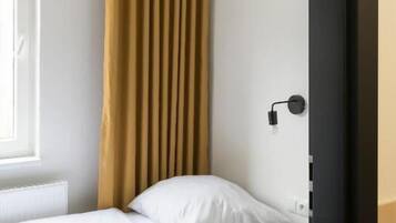 A single bed with a wooden frame, a white mattress, and a yellow pendant light.