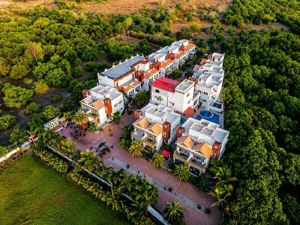 An aerial view of a residential complex with multiple buildings, a central courtyard, and surrounding greenery. - Aranya Villa Sasan Gir (Talala)