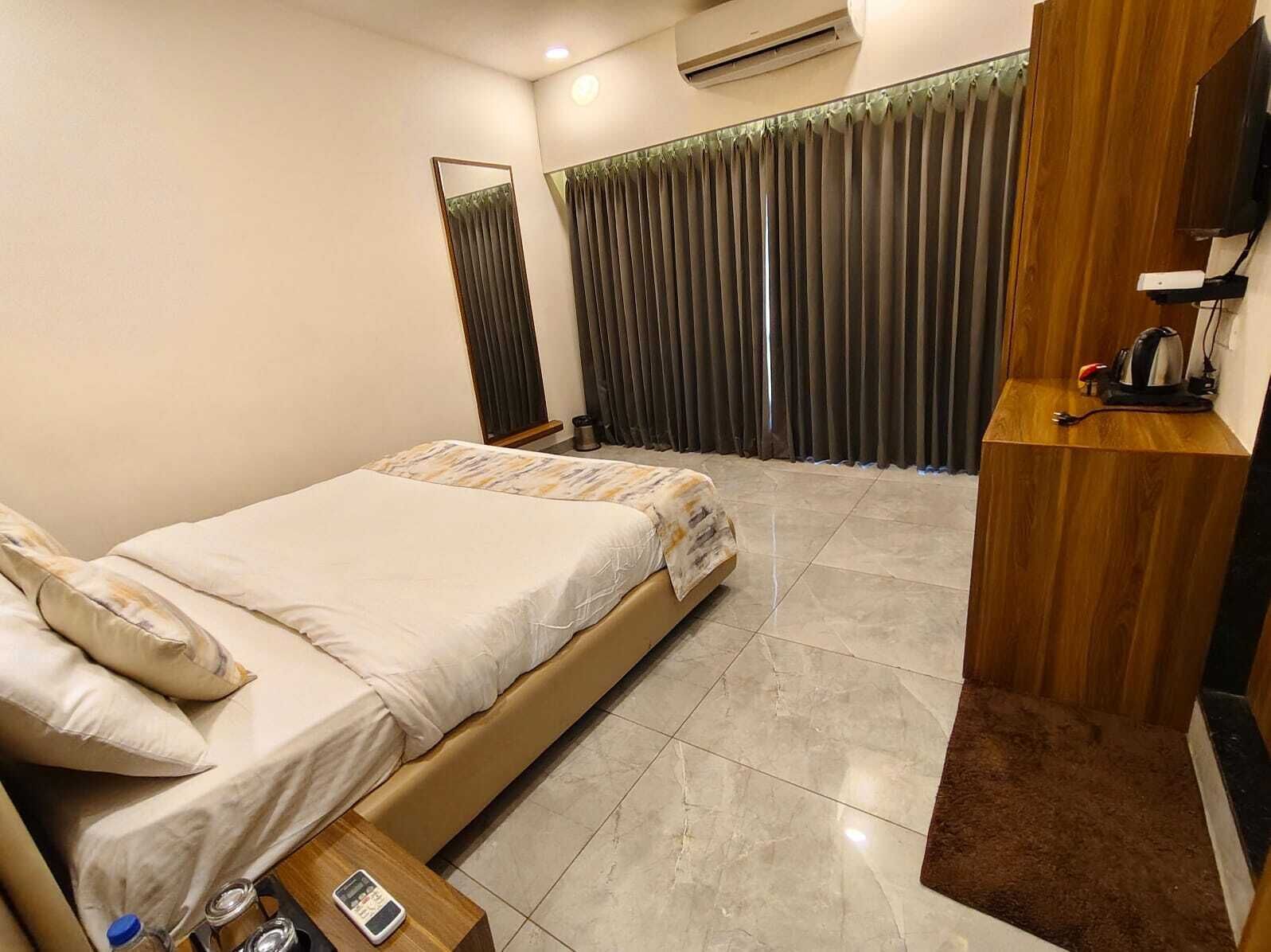 A hotel room with a bed, a wooden side table, a TV, and a window with curtains.