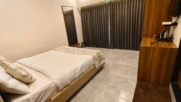 A hotel room with a bed, a wooden side table, a TV, and a window with curtains.