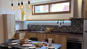 A modern kitchen with a dining area. It includes a wooden table with chairs, a built-in oven, and a window above the sink. - 3-bedroom house in Bananeiras in the center of Funchal (Funchal)