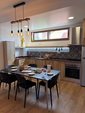 Eine moderne Küche mit Essbereich. Sie umfasst einen Holztisch mit Stühlen, einen Einbauofen und ein Fenster über der Spüle.