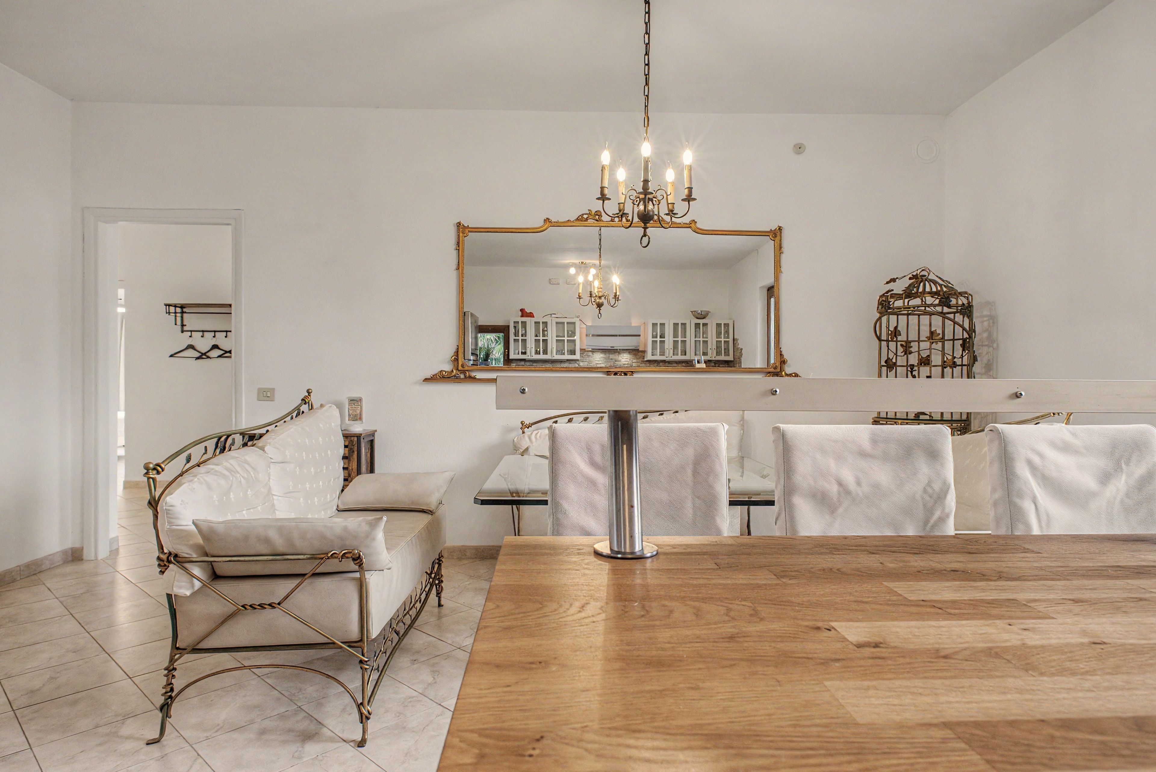 Un coin repas avec une table en bois, des chaises à revêtement blanc, un lustre et un grand miroir au-dessus de la table.