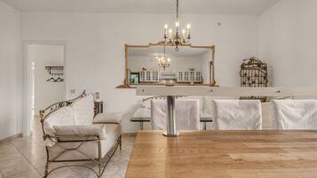 Un coin repas avec une table en bois, des chaises à revêtement blanc, un lustre et un grand miroir au-dessus de la table.