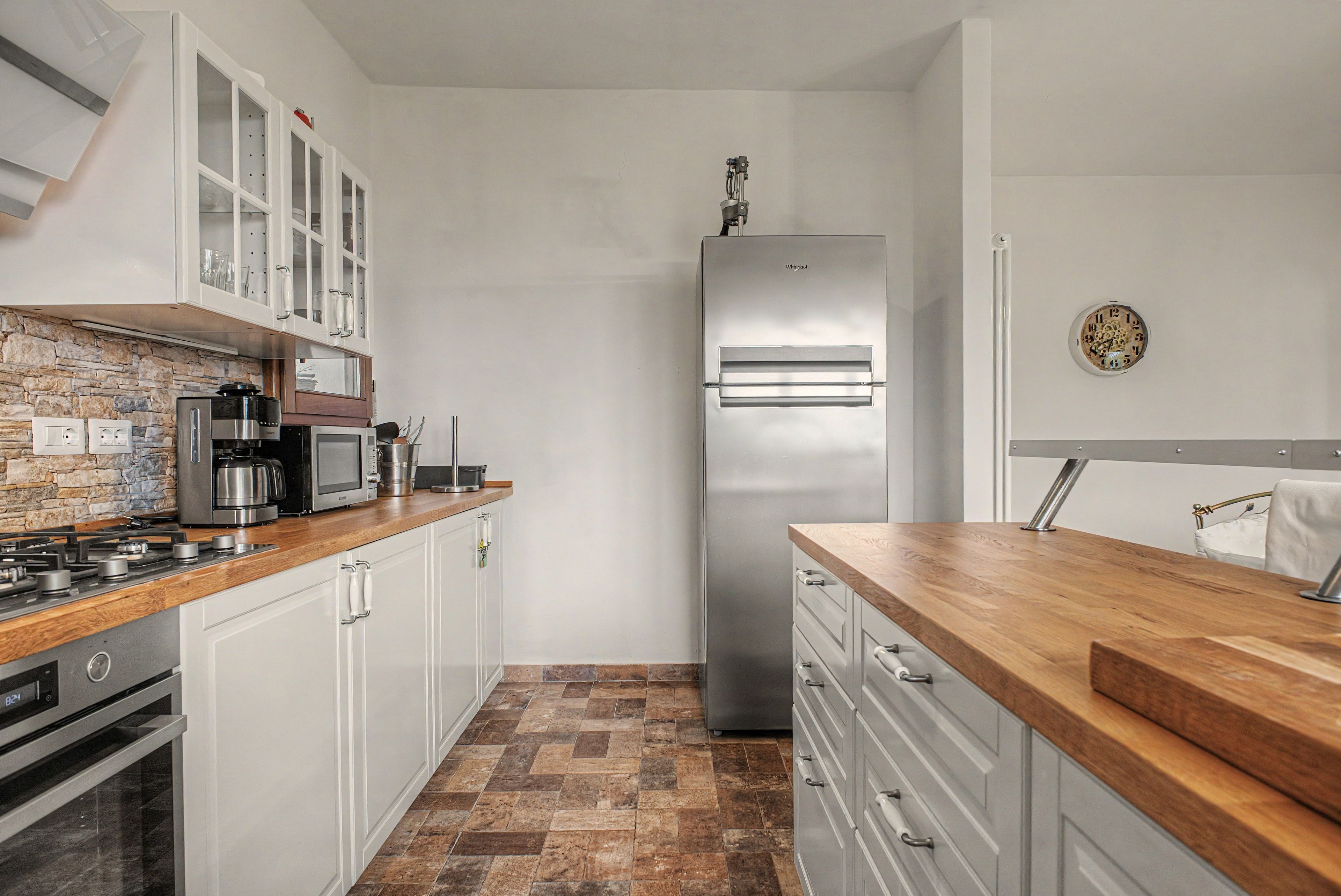 Een kleine keuken met witte kastjes, een koelkast van roestvrij staal en een houten aanrecht.