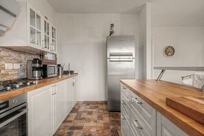 Une cuisine compacte avec des meubles blancs, un réfrigérateur en acier inoxydable et un plan de travail en bois.