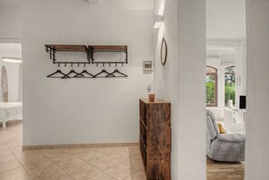 Un couloir avec un porte-manteau, une armoire en bois et une vue sur un salon comprenant un canapé et une fenêtre.