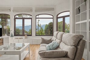 Un salon moderne avec un canapé, une table basse et une vue sur un paysage montagneux, visible à travers de grandes fenêtres en arc de cercle.