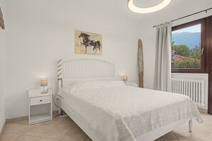 Een slaapkamer met een bed, nachtkastjes, een schilderij, een raam met gordijnen en uitzicht op het landschap.