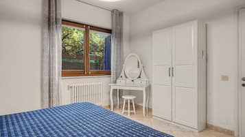 Une chambre à coucher comprenant un lit, une commode, une coiffeuse avec un miroir et une fenêtre donnant sur un paysage verdoyant.
