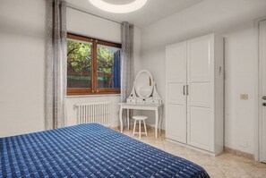 A bedroom with a bed, a dresser, a vanity with a mirror, and a window with a view of greenery. - Casa Paradiso in Porto Valtravaglia (Porto Valtravaglia)
