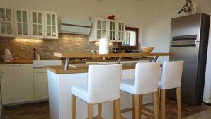 A kitchen with white cabinets, a wooden island with bar stools, a stainless steel refrigerator, and a stone backsplash. - Casa Paradiso in Porto Valtravaglia (Porto Valtravaglia)