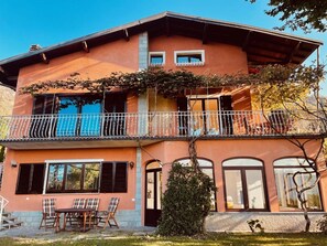 Ein zweistöckiges Gebäude mit einem Balkon, einem Essbereich mit Stühlen und einem Tisch sowie einer Tür mit einem Rundbogenfenster.
