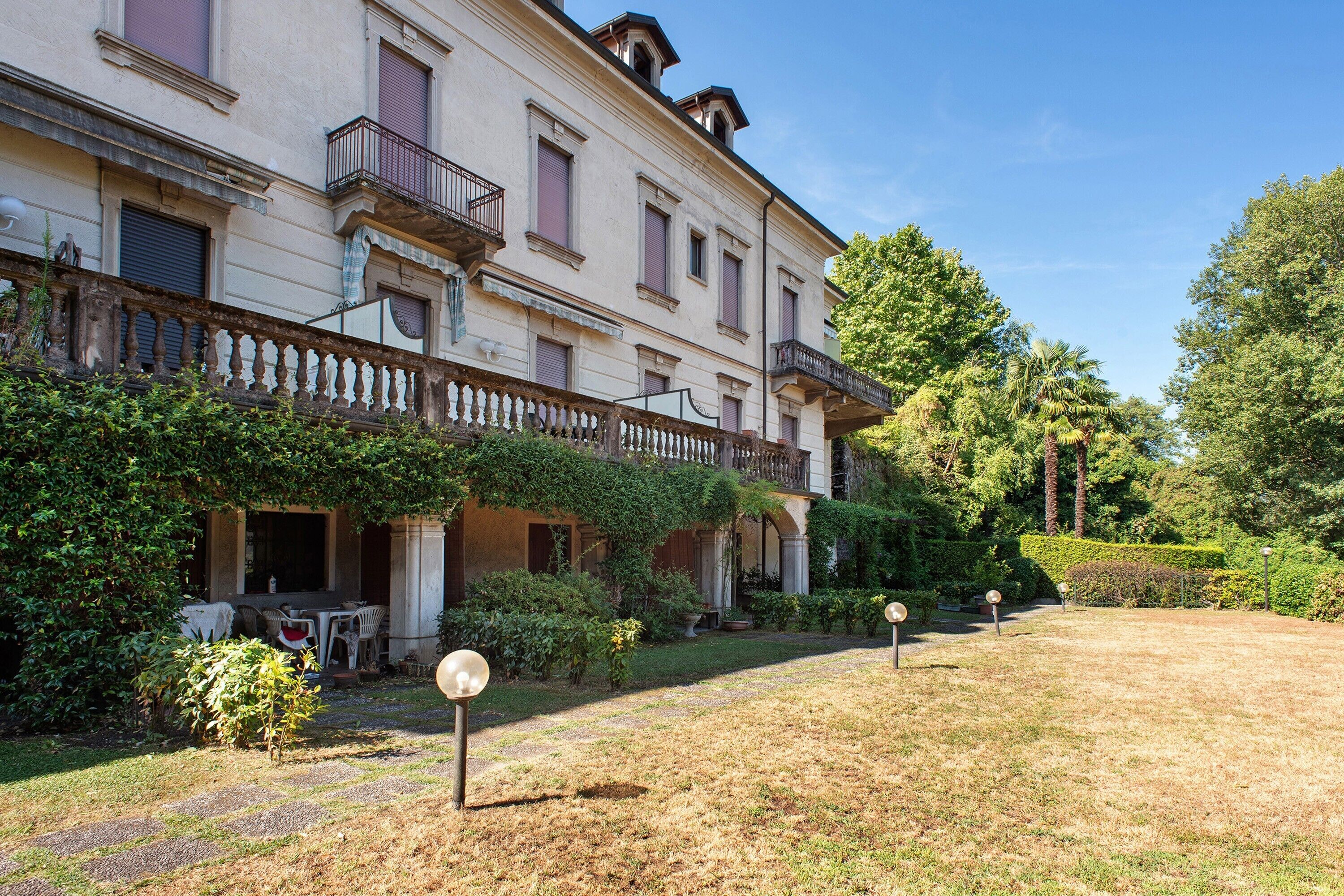 A large building with a balcony, a covered patio, and a well-maintained garden.