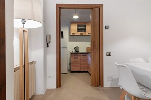 A narrow hallway leading to a kitchen with wooden cabinets, a white table, and a lamp. - Casa Corsini in Porto Valtravaglia – Lake View Apartment (Porto Valtravaglia)
