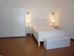 Une chambre à coucher comprenant un lit, des tables de chevet, un banc et une armoire.