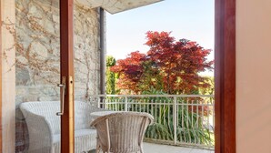 Ein Balkon mit Korbmöbeln, einer Steinmauer und Blick auf Bäume.