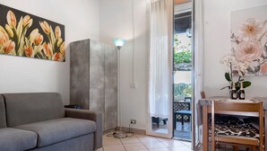 Ein Wohnzimmer mit einer Couch, einer Stehlampe, einem Esstisch mit Stühlen und einem Blumenbild an der Wand.