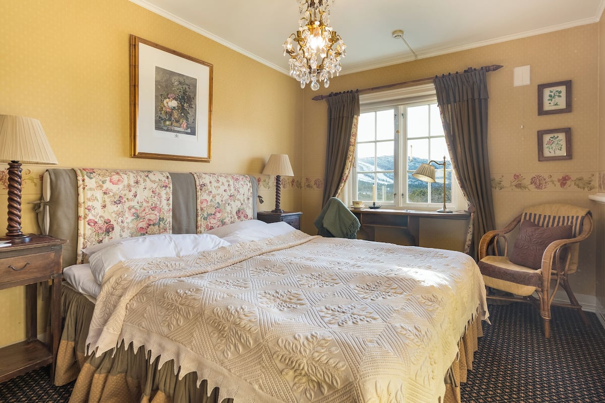 A hotel room with a large bed, a chair, a desk, and a window with curtains.